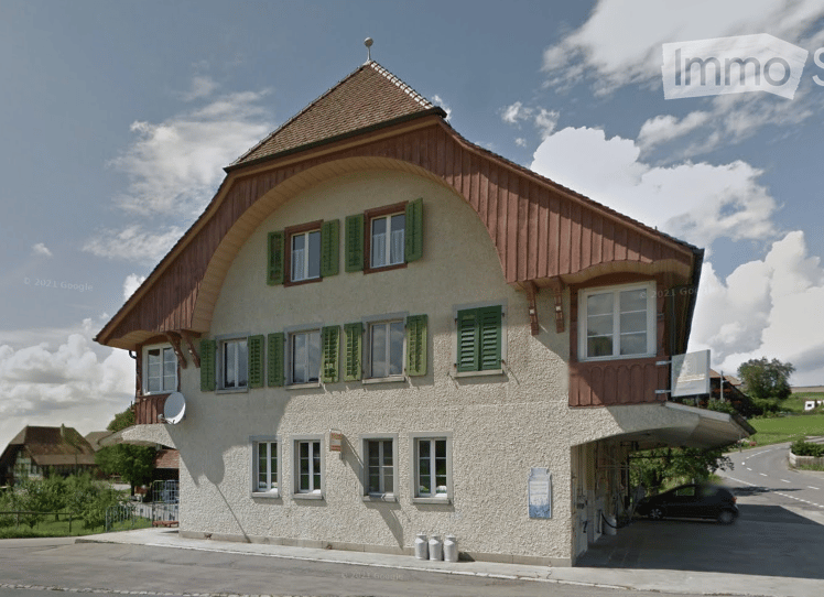 Traditional Swiss-style building with a pitched roof, green shutters, and a covered garage entrance.