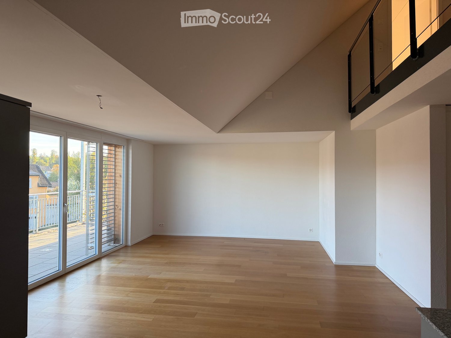 Empty room with wooden flooring, white walls, large sliding glass doors leading to a balcony, and a visible staircase leading to an upper level.