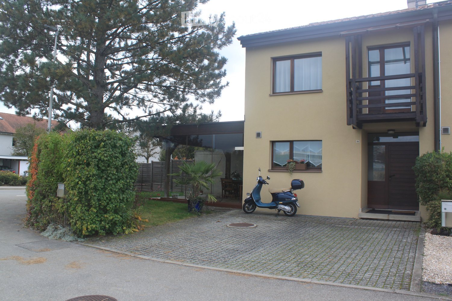 Two-story house with beige exterior, large windows, balcony, and a scooter parked in front.