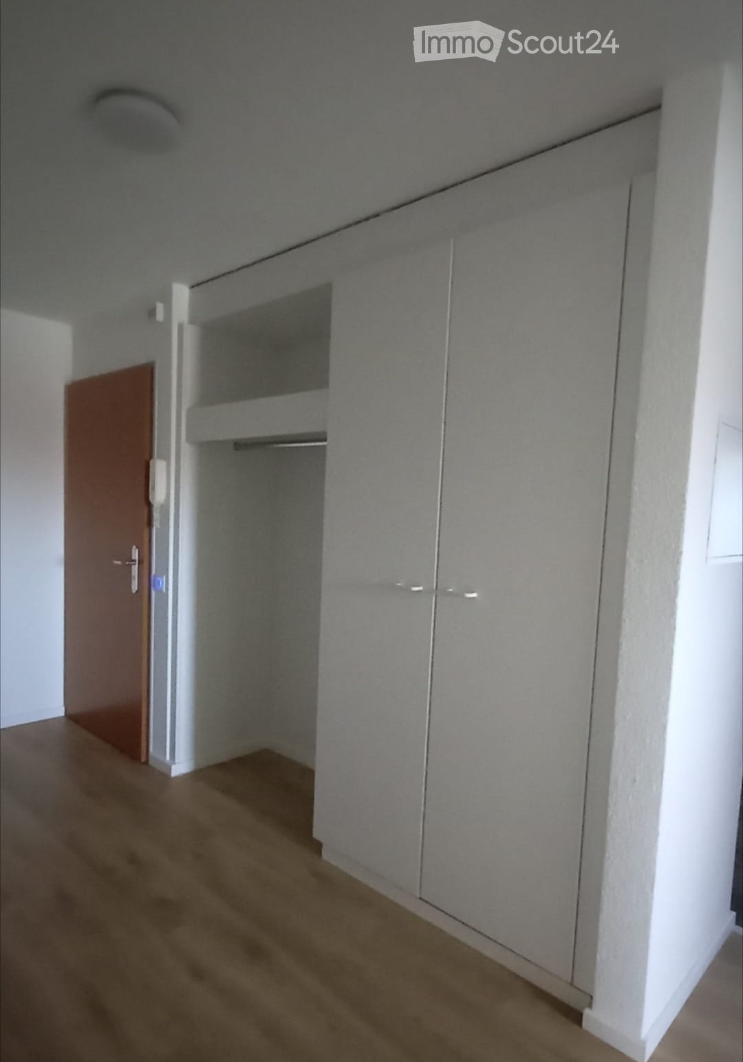 Empty room with light grey walls, wooden floor, and built-in closet with mirrored doors.