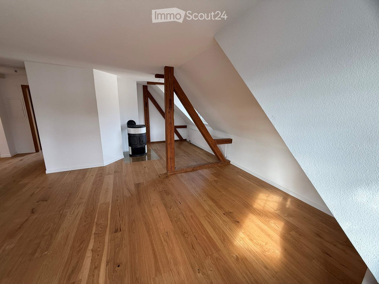 empty attic room with wooden flooring and white walls, wooden beam support and small waste bin in center