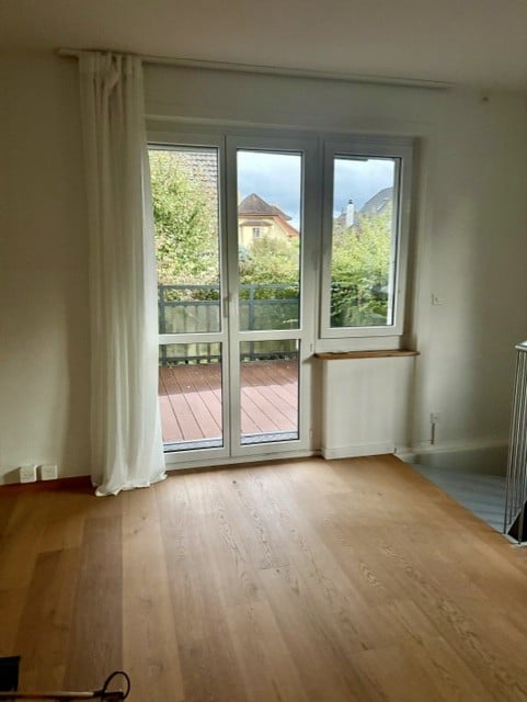 Empty room with wooden flooring, large glass sliding doors leading to a balcony, white walls, and a radiator.