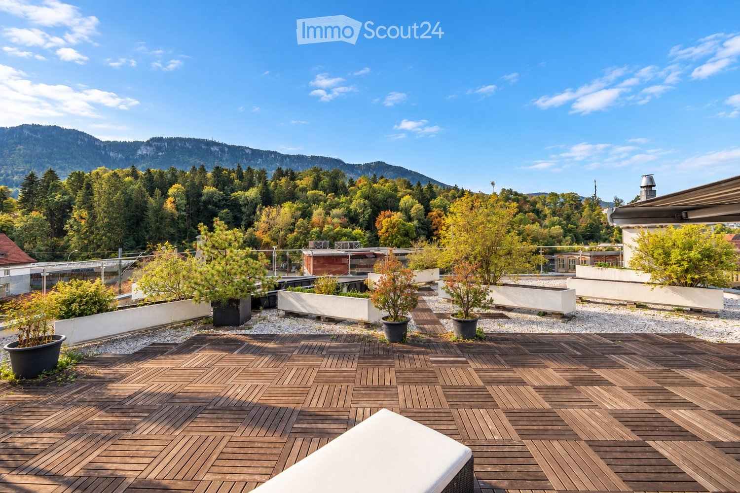 Rooftop terrace with wooden decking, potted plants, and a scenic mountain view.