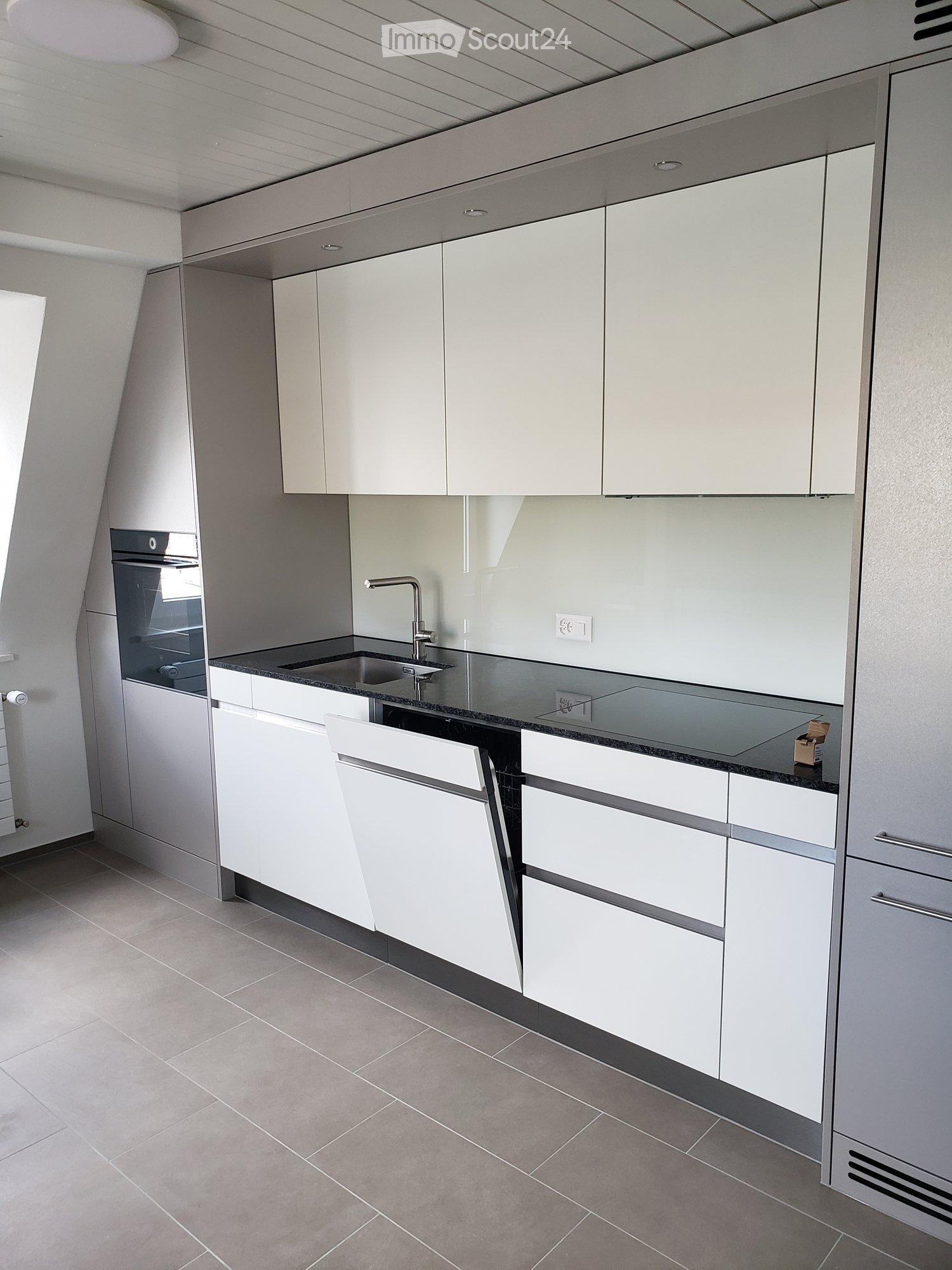 Modern kitchen with white cabinets, stainless steel sink, and built-in oven. Features a sleek design with a dark countertop and tiled floor.