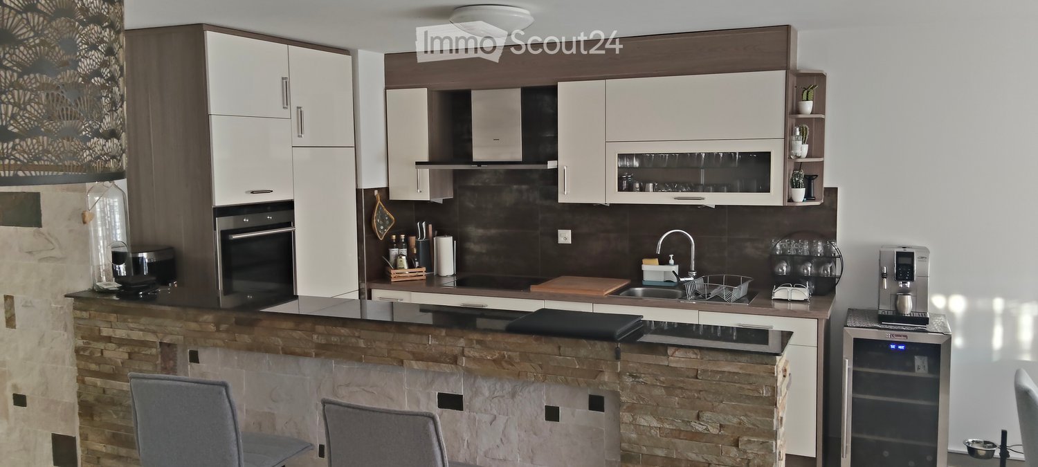 Modern kitchen with white cabinets, dark countertops, and a stone island. Includes a sink, faucet, oven, coffee maker, and stools.