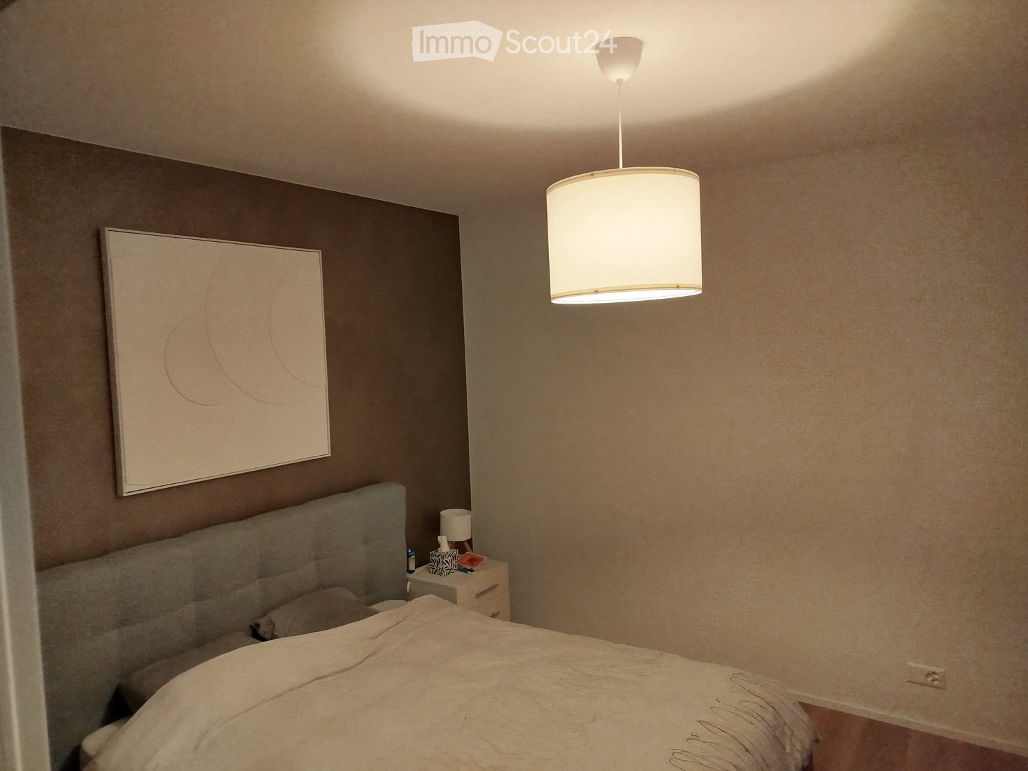 Modern bedroom with a large bed, nightstand, lamp, and a decorative picture frame on the wall.