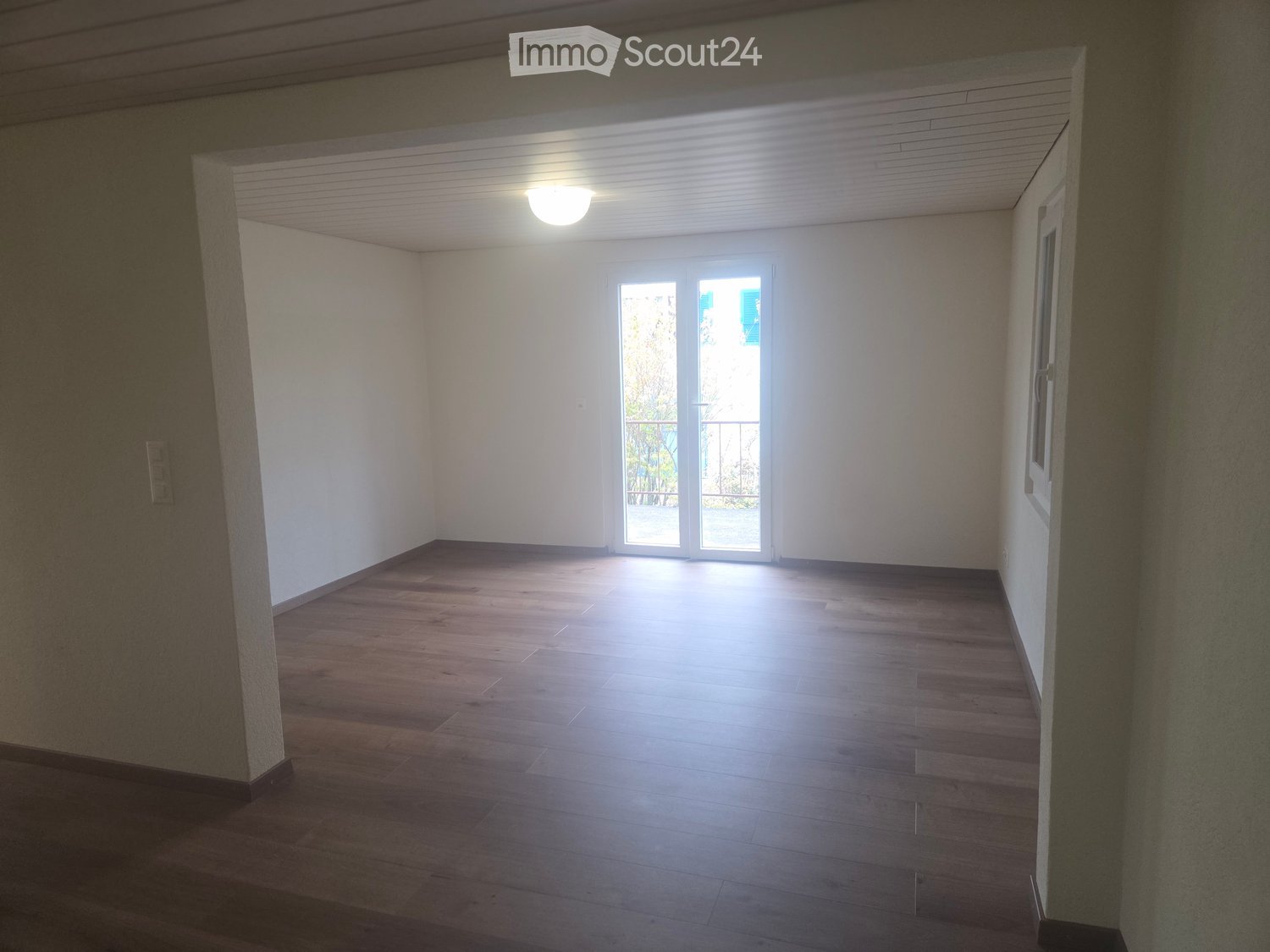 Empty room with wooden flooring, white walls, and large sliding glass doors leading to a balcony.