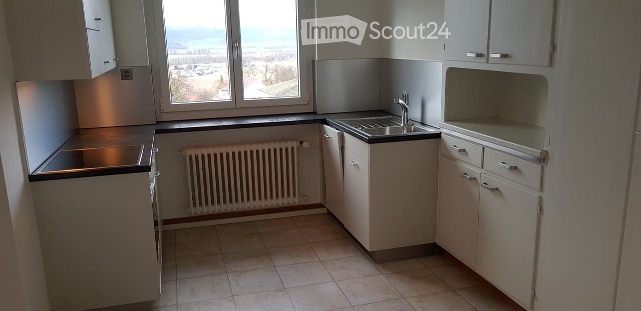 Modern kitchen with white cabinets, tiled floor, sink, faucet, and radiator under large windows offering a scenic view.