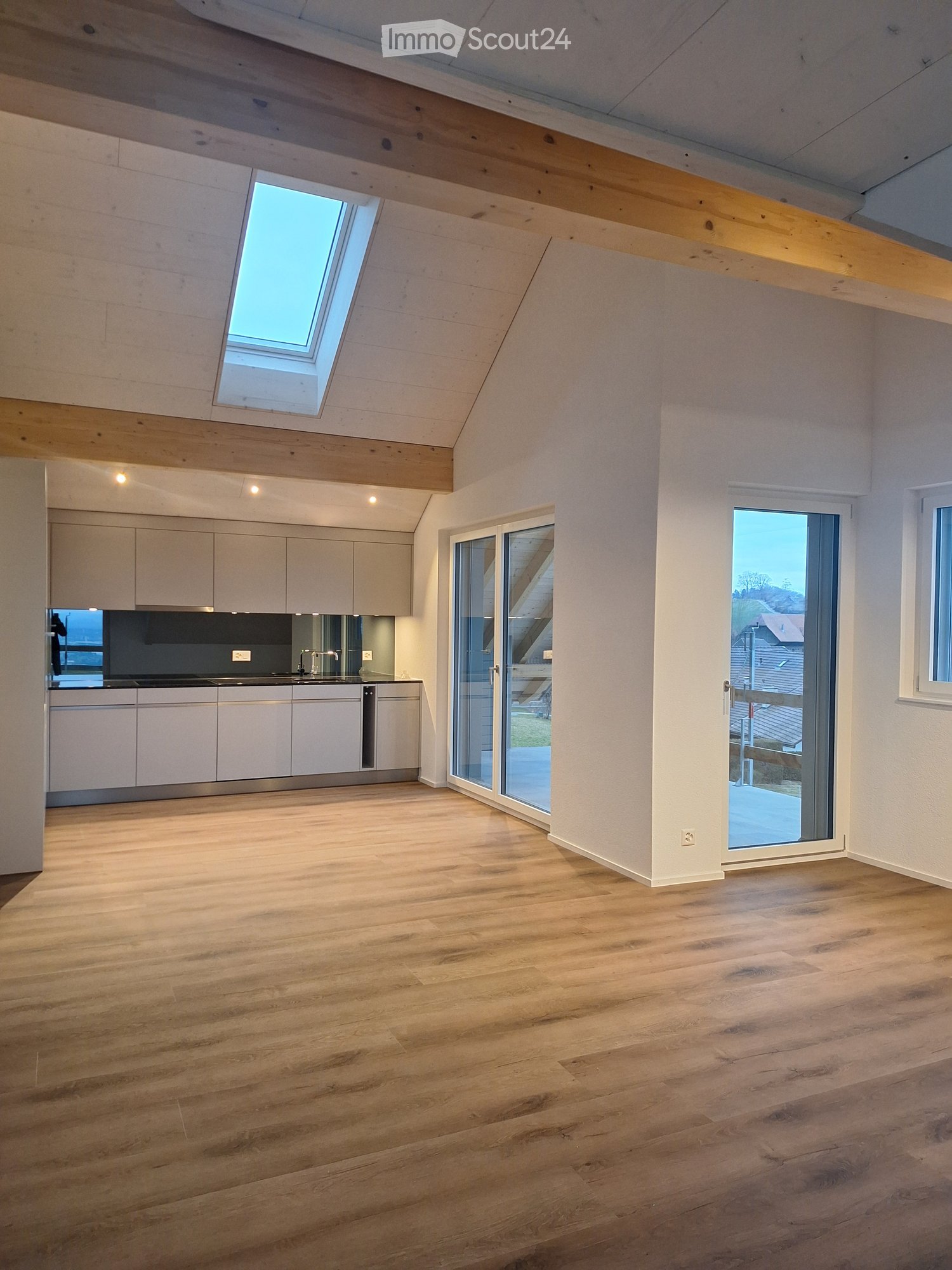 Bright, open kitchen with light wood flooring, white cabinets, and large windows, including a skylight and sliding glass doors leading to a balcony.