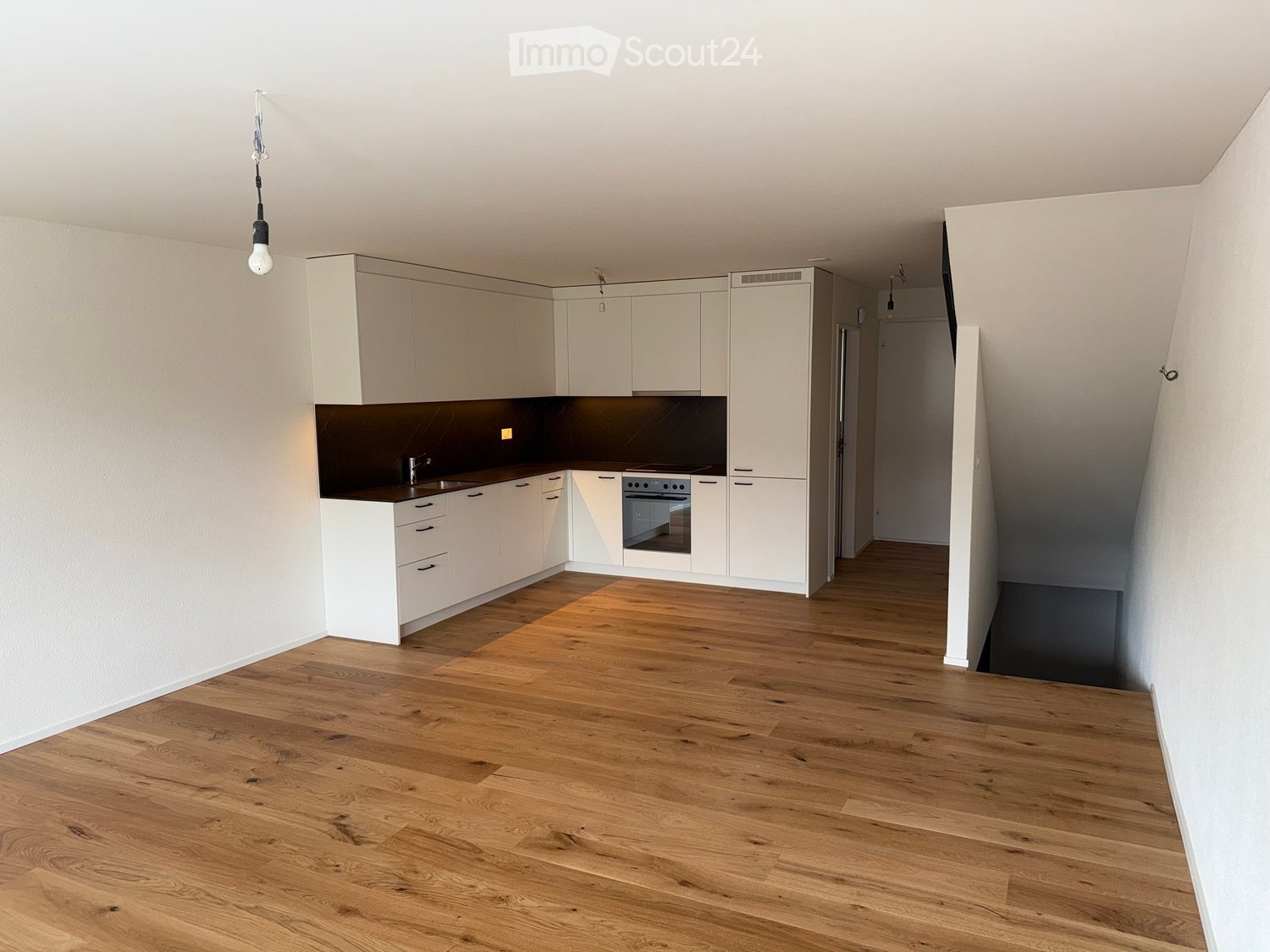 Empty kitchen with white cabinets, dark countertop, and wooden flooring. No furniture or appliances are present.