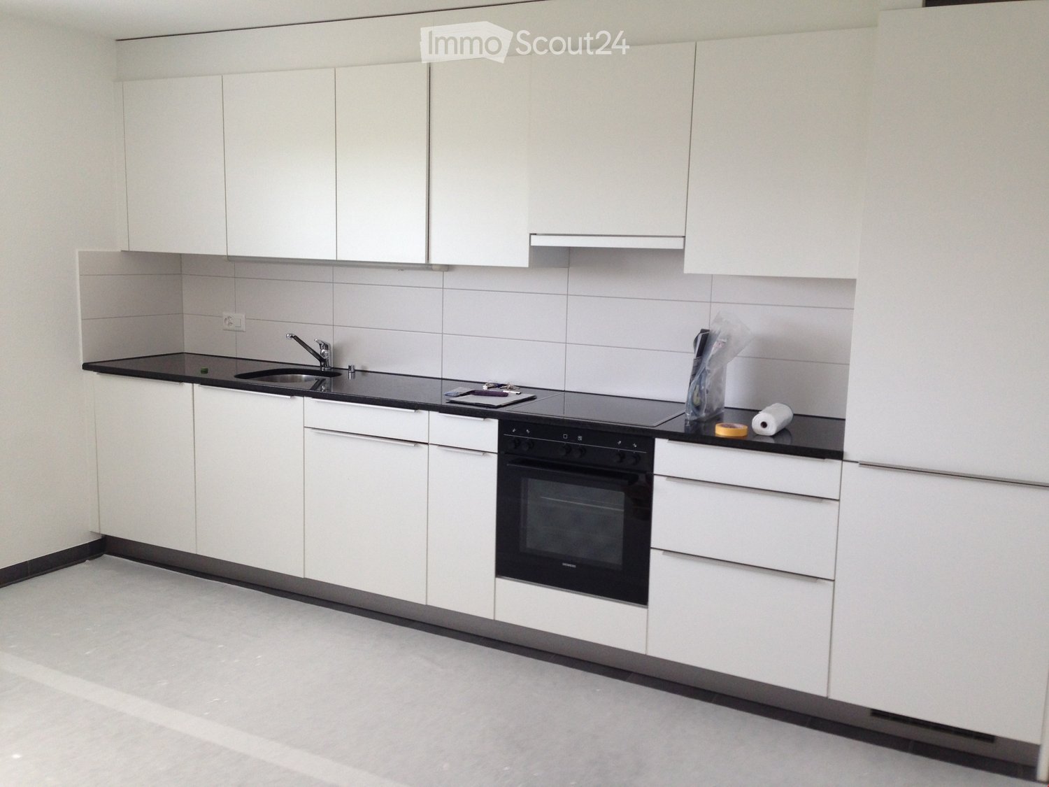 Modern kitchen with white cabinets, black countertops, and built-in oven. Includes sink, faucet, and various kitchen items on the counter.