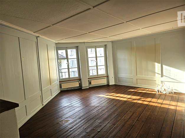 Empty room with wooden flooring, white walls, and two windows with radiators beneath them. No furniture or equipment present.