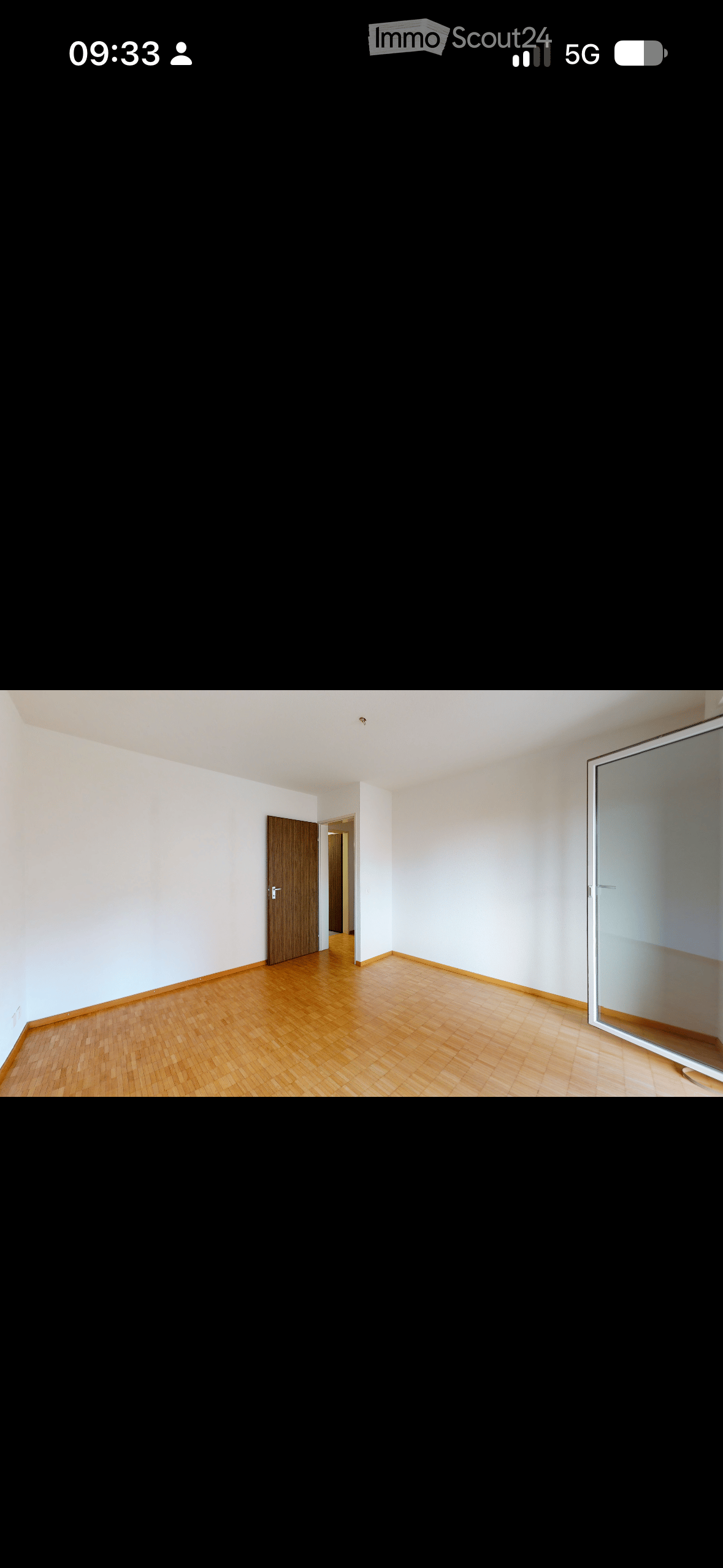 Empty room with wooden flooring, white walls, and a wooden door leading to another room.