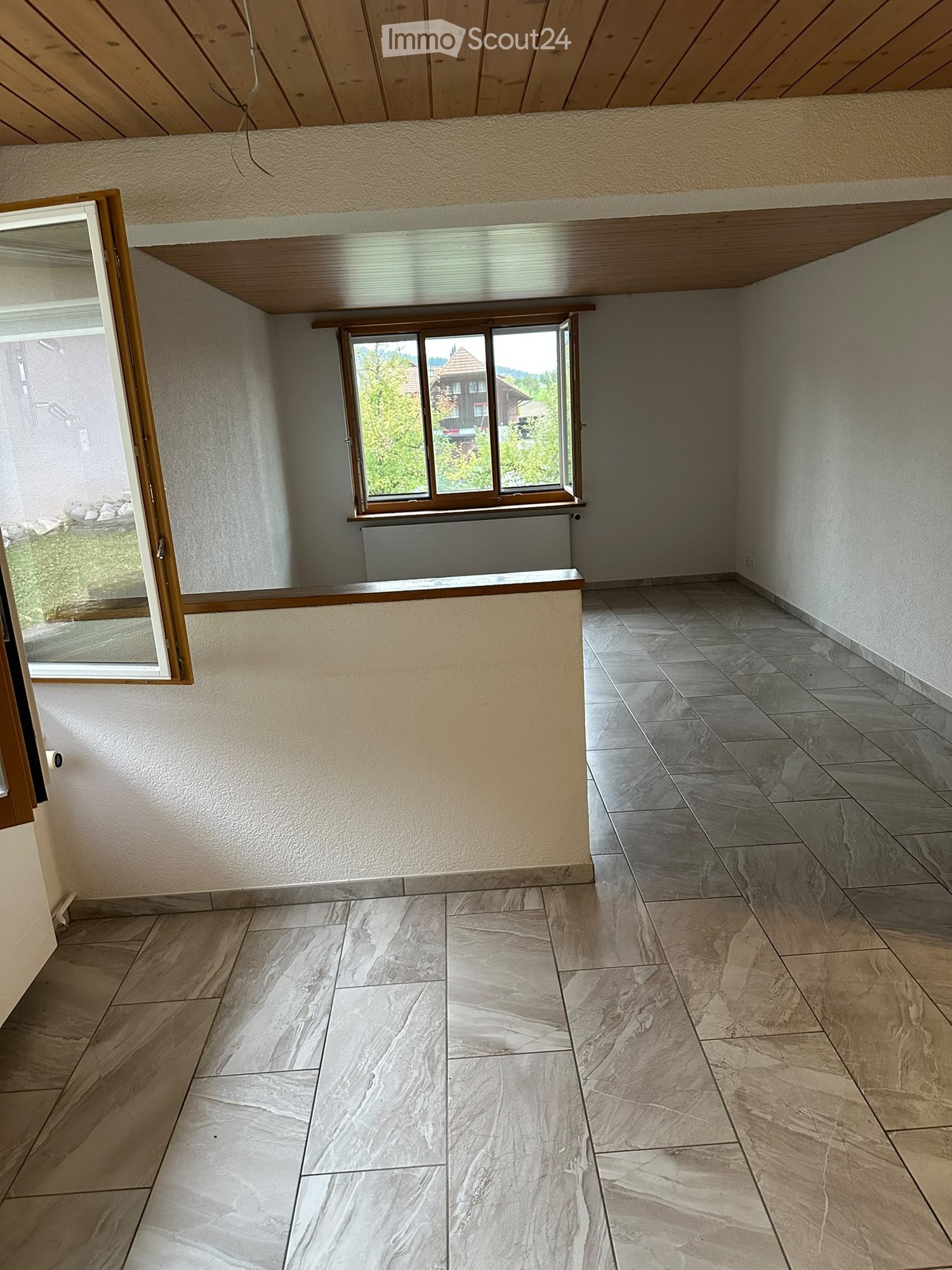 Empty room with tiled flooring, wooden ceiling, and large windows offering a view of the outdoors.