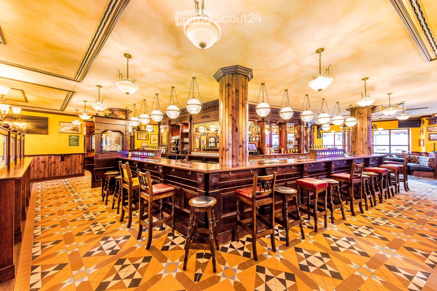 A well-furnished bar area with a long wooden bar counter, multiple bar stools, pendant lights, shelves stocked with bottles, and a cozy seating area with a sofa.