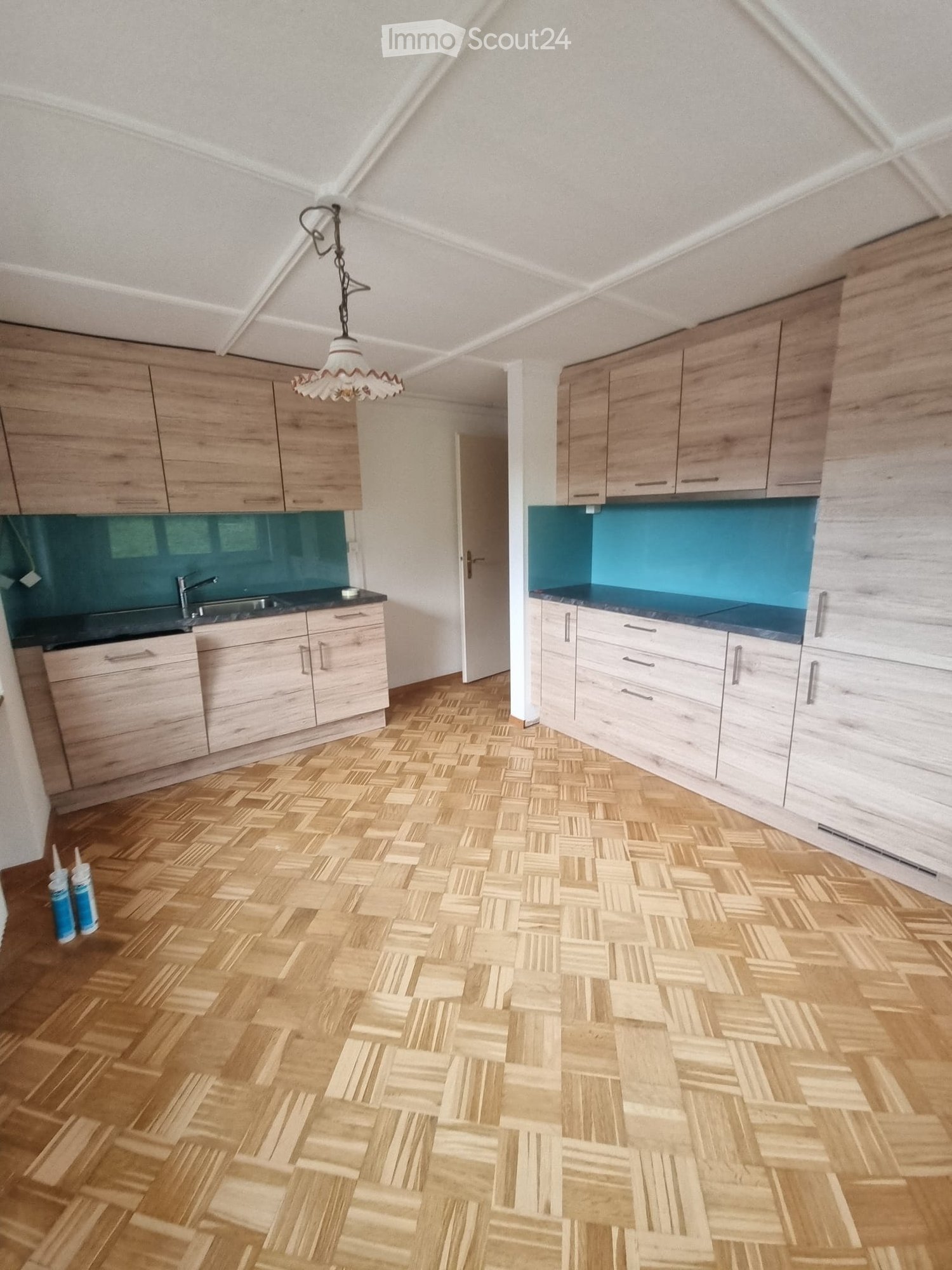 Empty kitchen with wooden floor, wooden cabinets, blue countertops, a sink, and a faucet