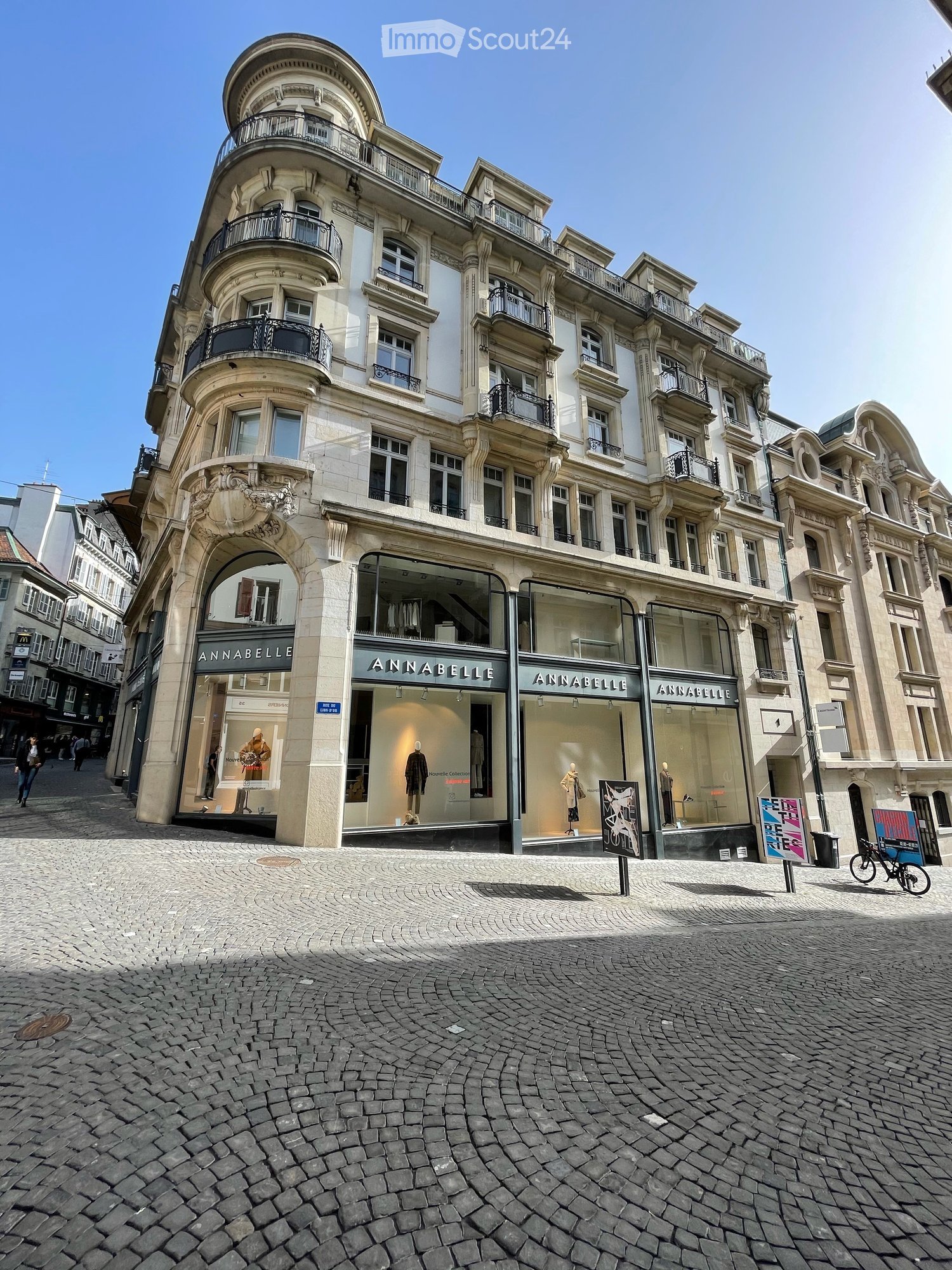 Multi-story building with ornate architecture, large windows, and balconies. The ground floor features a storefront with glass windows displaying mannequins and clothing.