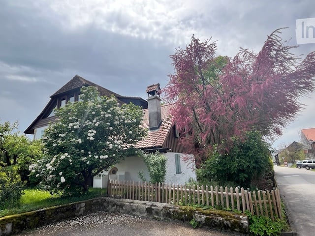 traditional house with brown roof, white walls, wooden fence, chimney, garden, trees, shrubs