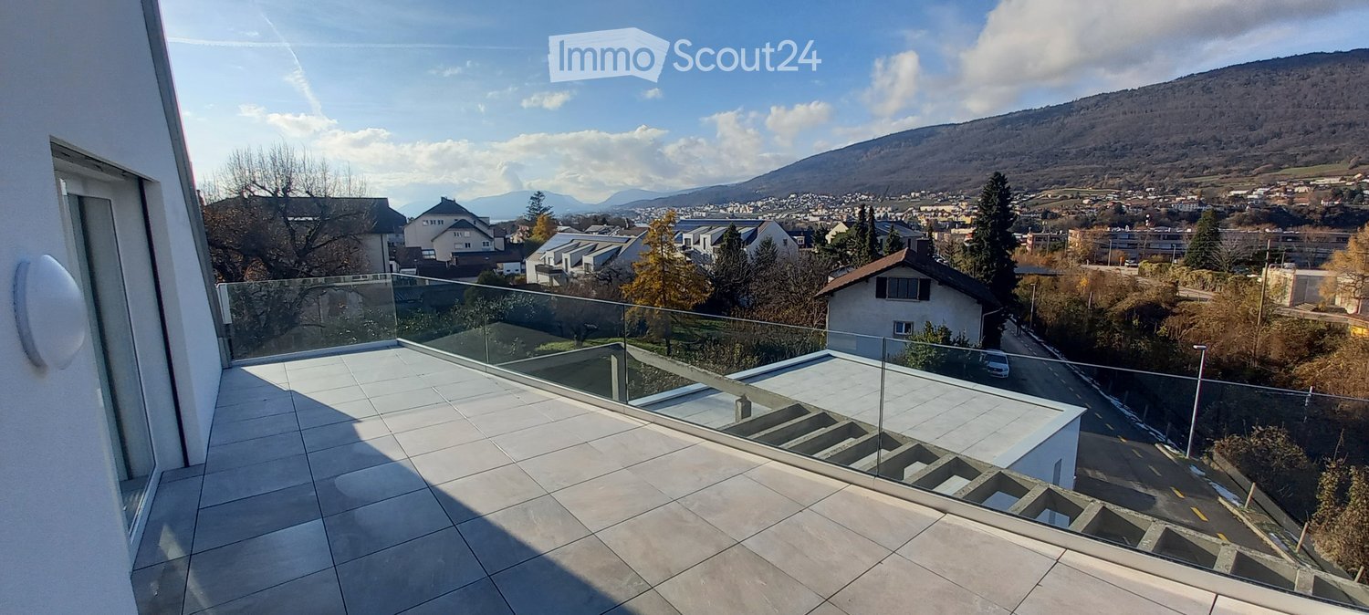 Modern balcony with glass railing, tiled floor, and scenic city and mountain view.
