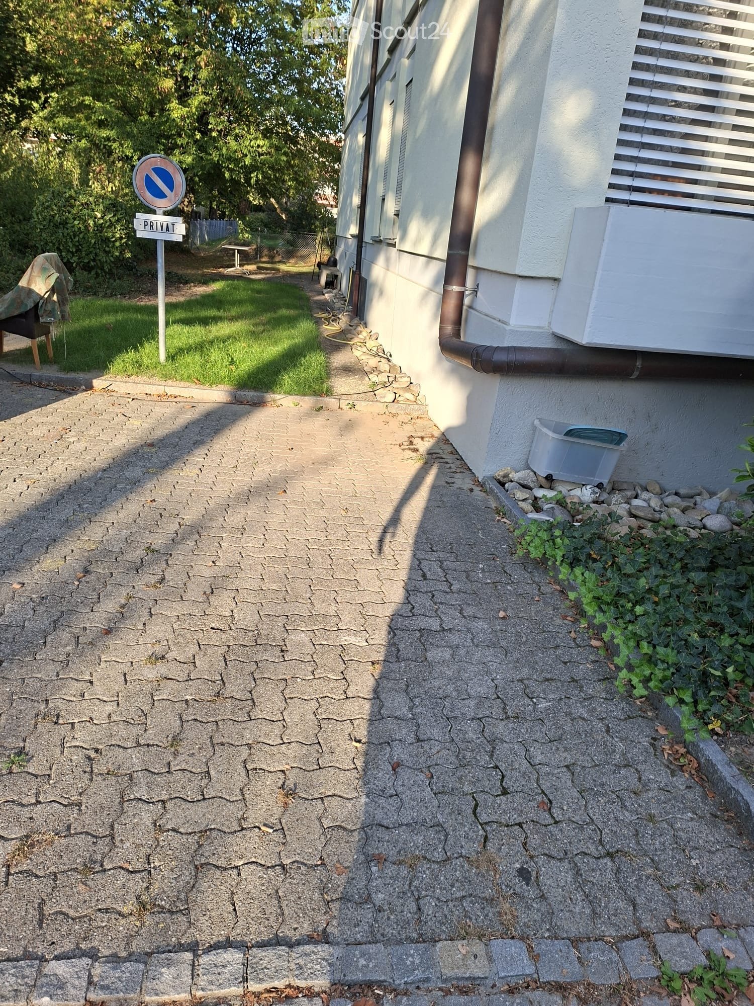 A pathway leading to a house with a cracked concrete surface, a small garden area, and a "PRIVAT" sign indicating a private property.