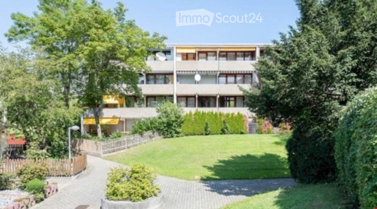Multi-story residential building with balconies, surrounded by a well-maintained lawn and trees.
