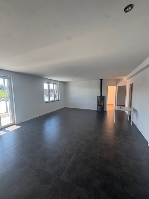 Empty room with dark tiled floor, white walls, large windows, and a fireplace in the corner.