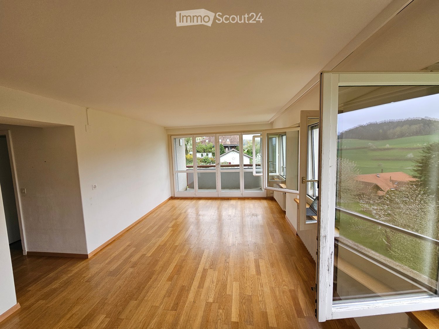 Empty room with wooden flooring, large windows, and a view of a green landscape.
