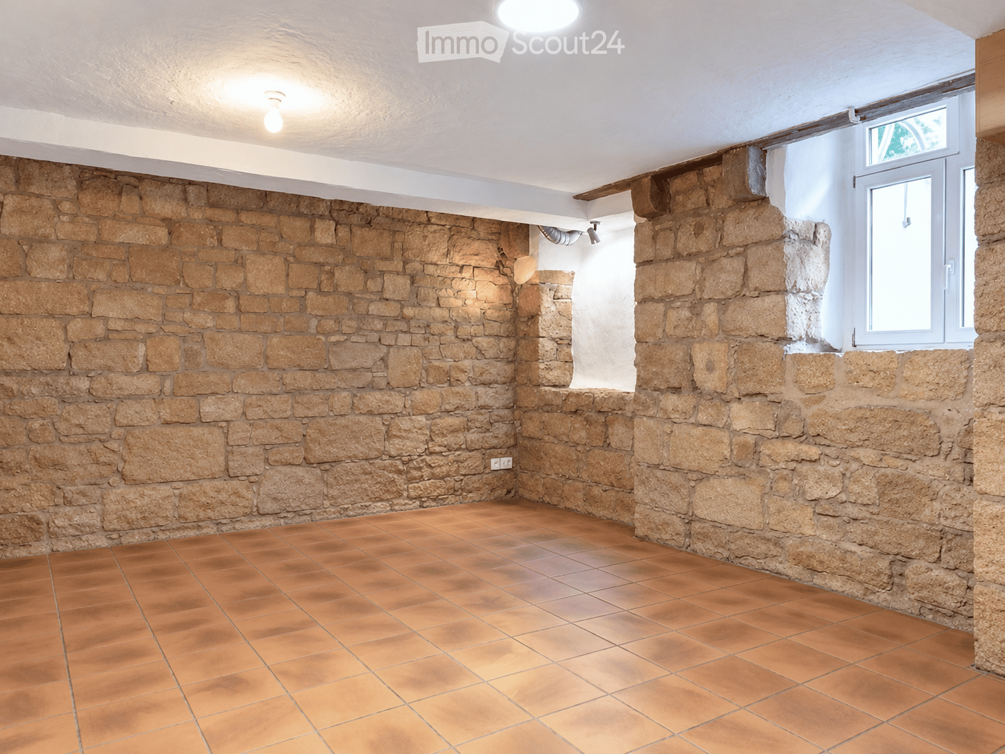 Empty room with stone walls and terracotta tiled floor, featuring a small window and recessed lighting.
