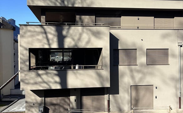 Modern two-story building with a balcony and large windows, featuring a clean, minimalist design with neutral tones and a flat roof.