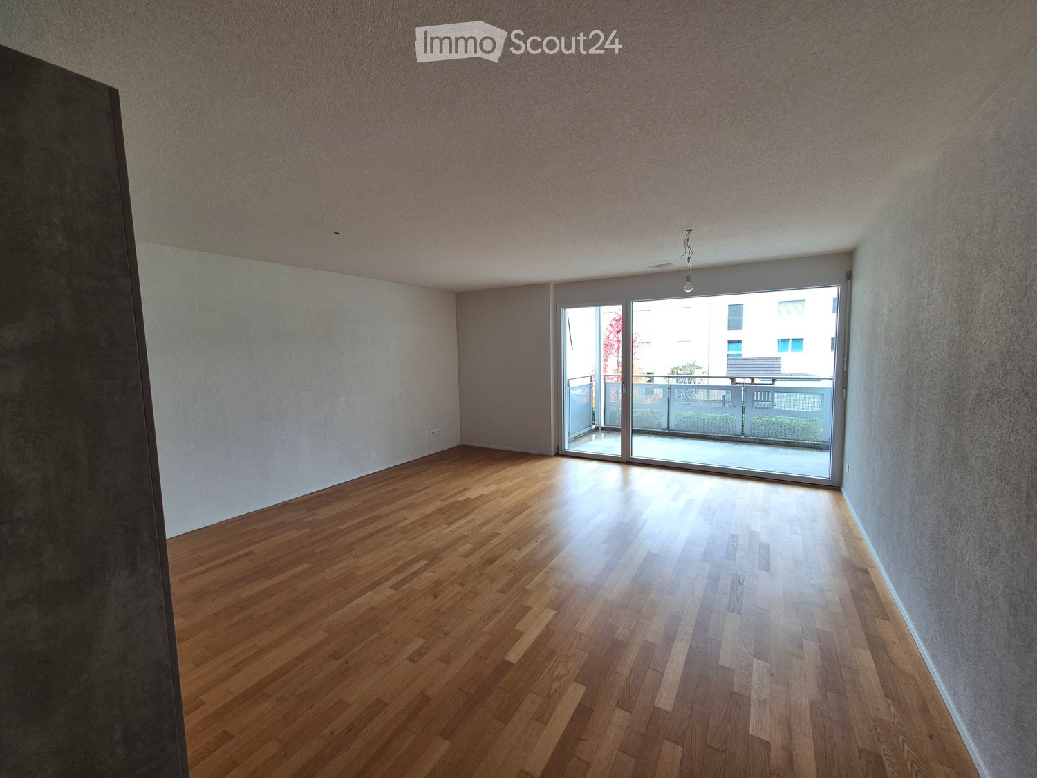 Empty room with wooden flooring, white walls, and a large sliding glass door leading to a balcony.