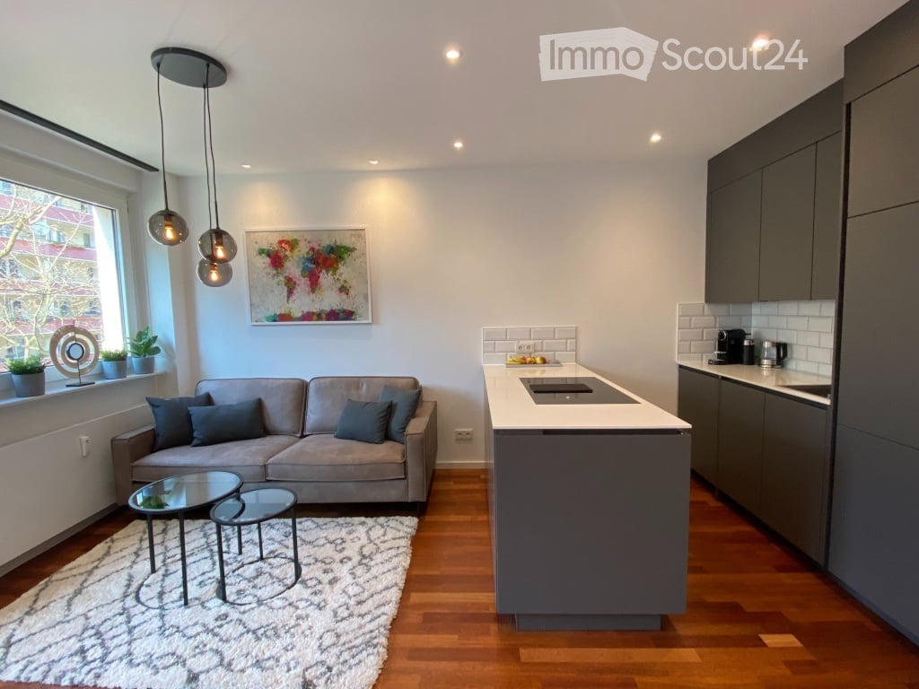 Modern open-plan living and kitchen area with grey sofa, coffee table, small side table, kitchen island, and pendant lights.