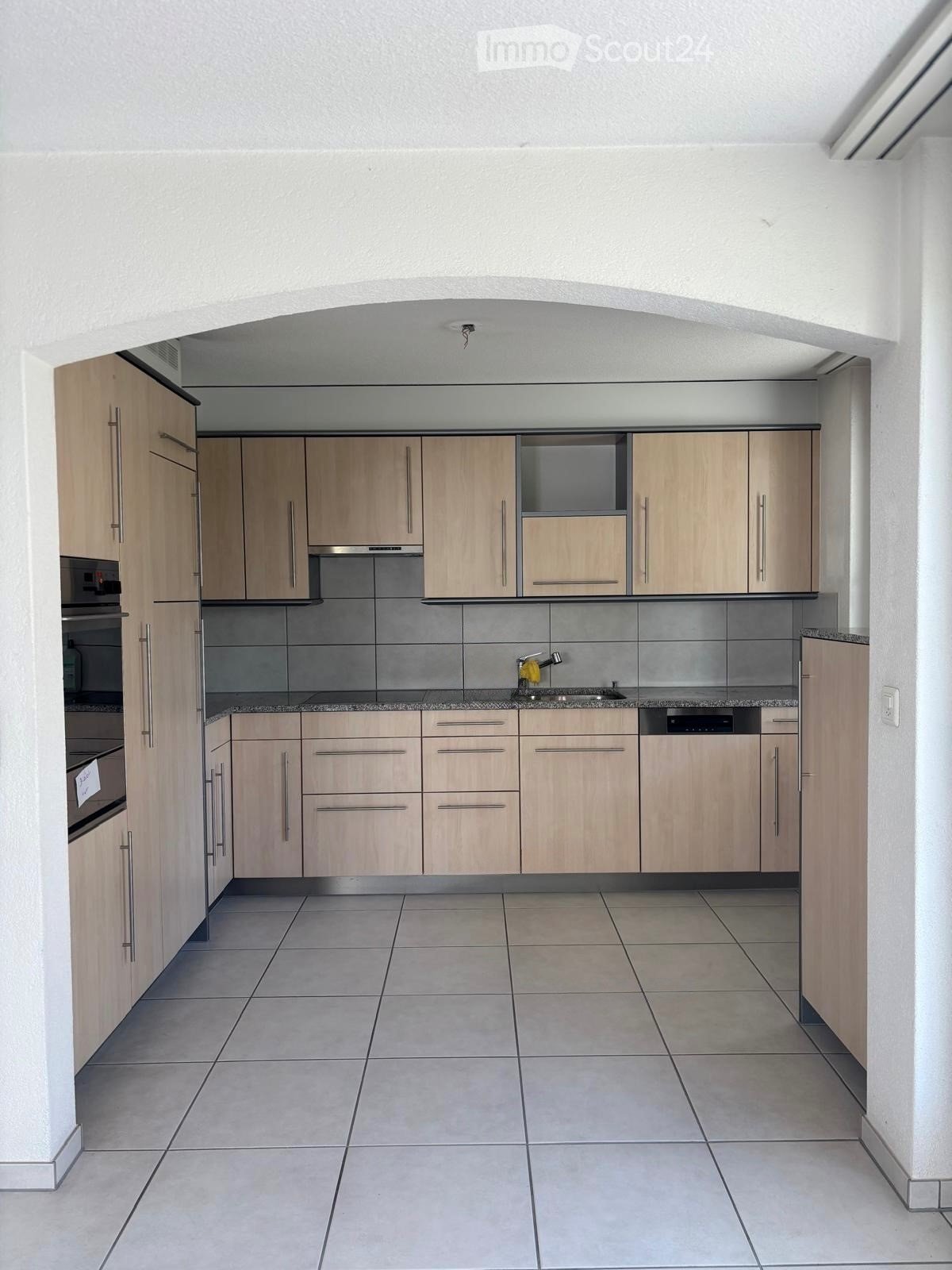 Modern kitchen with light wood cabinets, stainless steel appliances, and tiled flooring.