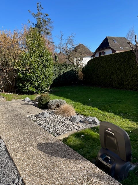 well-maintained green lawn, pathway, rocks, plants, and hedges, house in the background, clear sky
