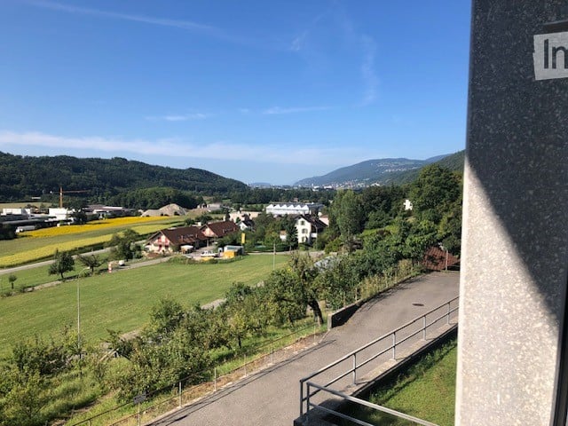Balcony overlooking a rural landscape with fields, trees, and distant buildings.