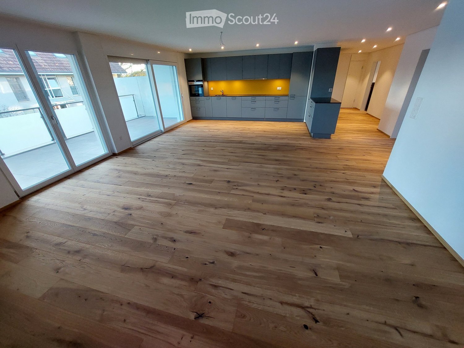 Empty room with wooden flooring, grey cabinets, and large sliding glass doors leading to an outdoor area.