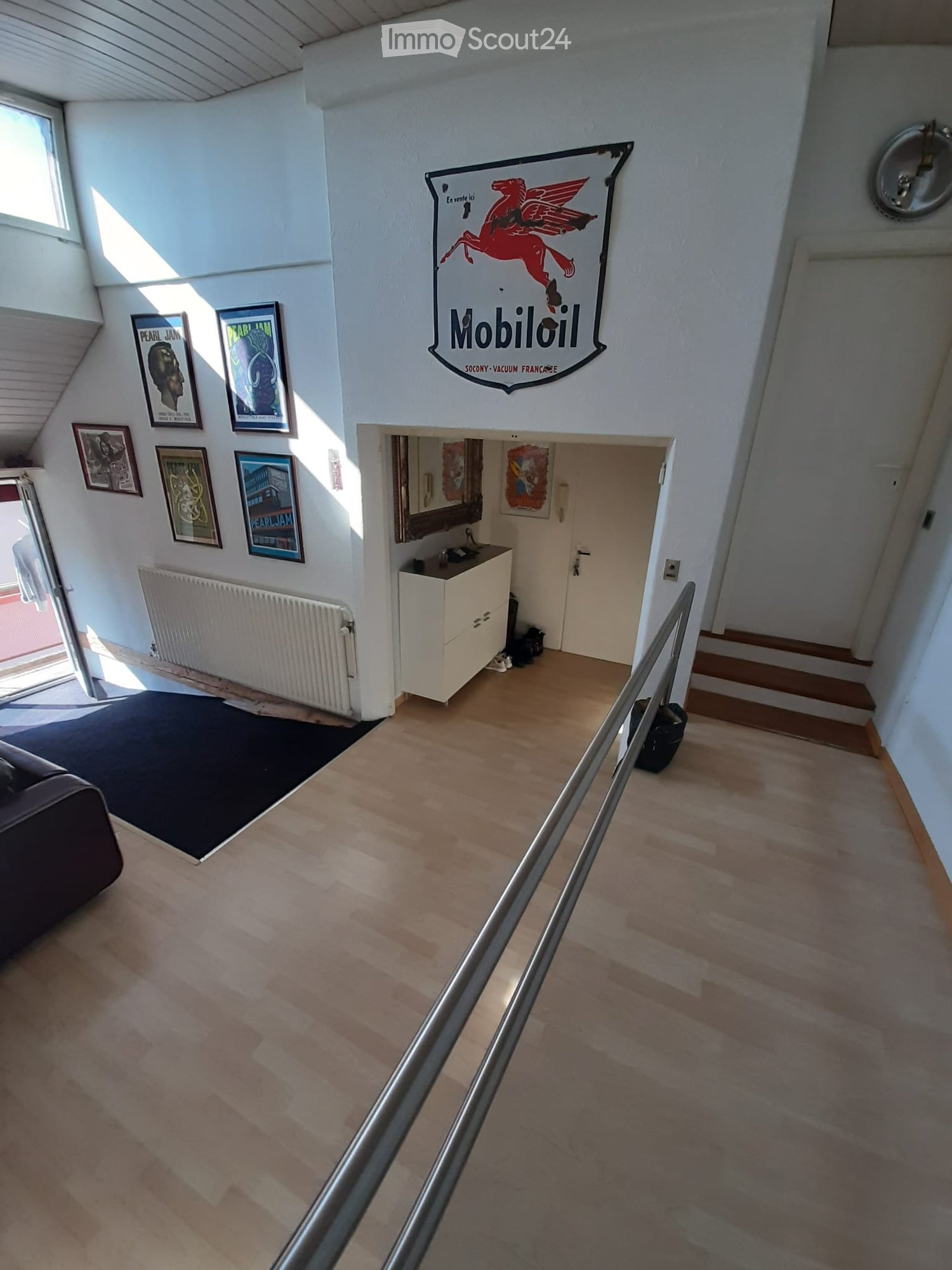 A modern hallway with wooden flooring, a staircase, a sofa, radiator, sink, and framed pictures on the wall.