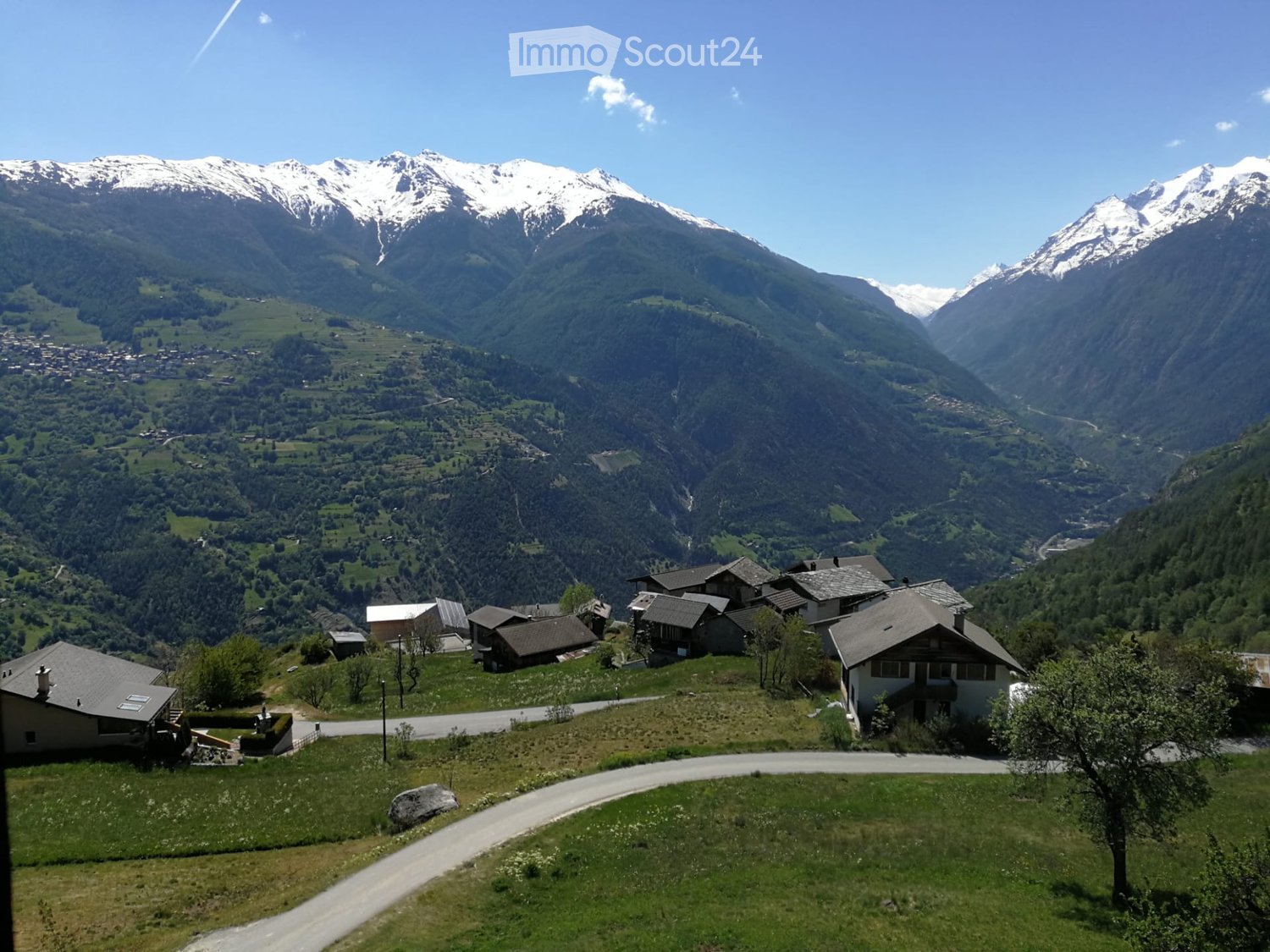 A cluster of houses in a valley surrounded by mountains, with a winding road leading through the area.