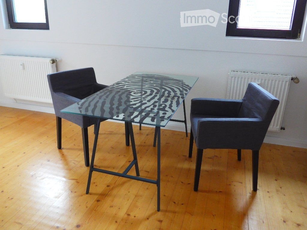 A modern, minimalist room with a glass table and two dark blue chairs, wooden flooring, and white walls.