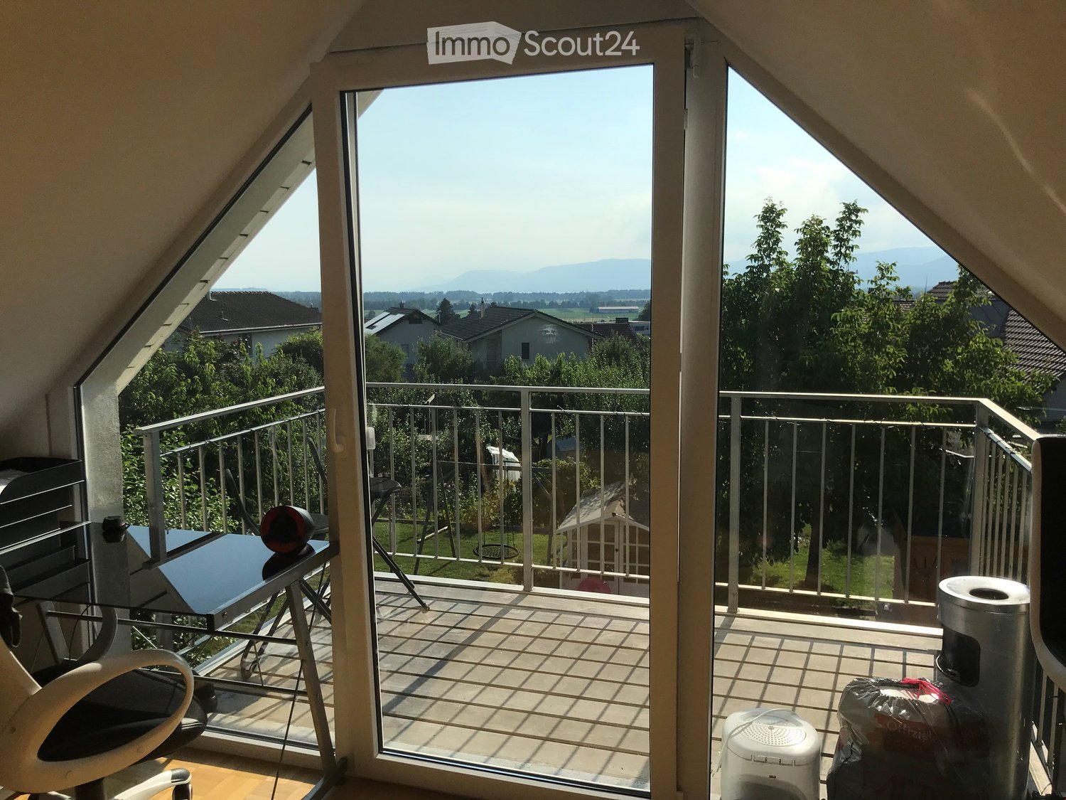 Large balcony with railings, balcony table and chairs, office chair, glass doors, mountain view