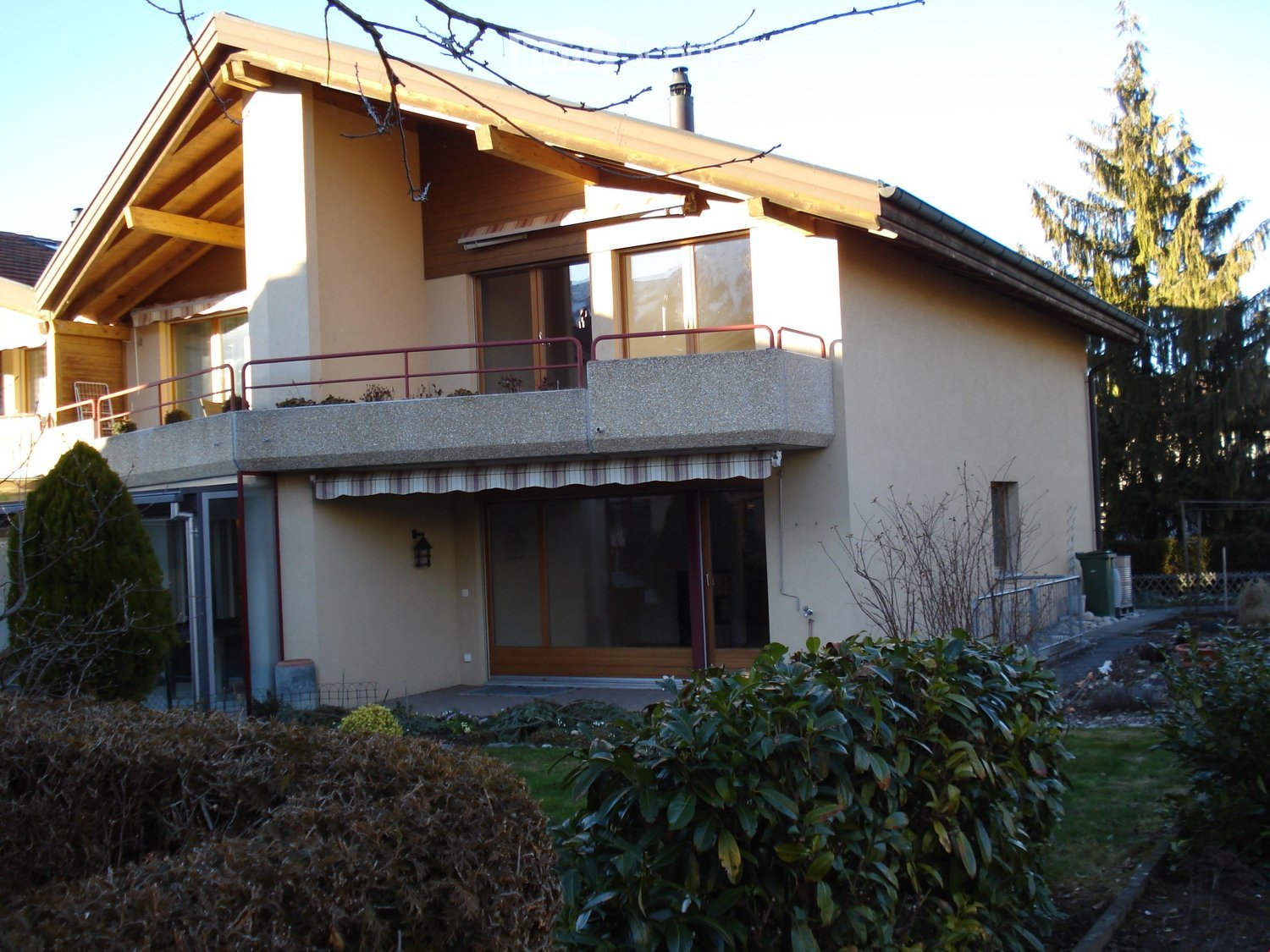Two-story house with a balcony, large windows, and a well-maintained garden.