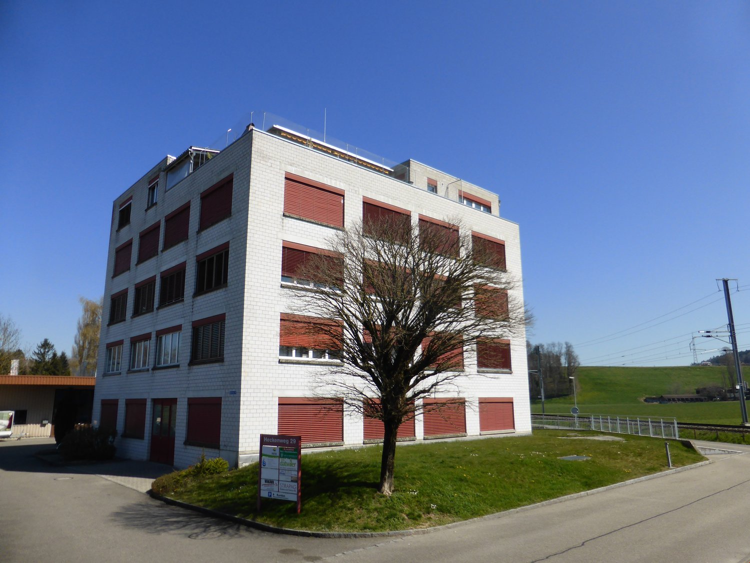 Building: multiple windows, red doors, signboard, grassy area, street