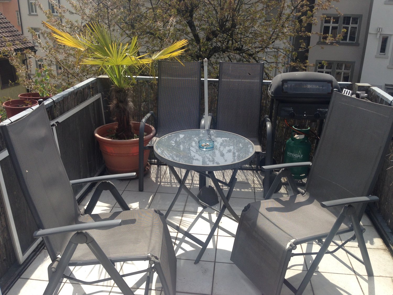 Gray reclining chairs with a round glass table and a barbecue on the balcony
