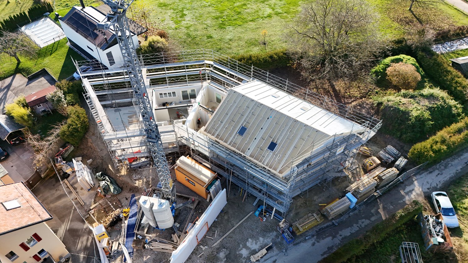 Aerial view of an under-construction building with scaffolding, crane, and surrounding construction materials.
