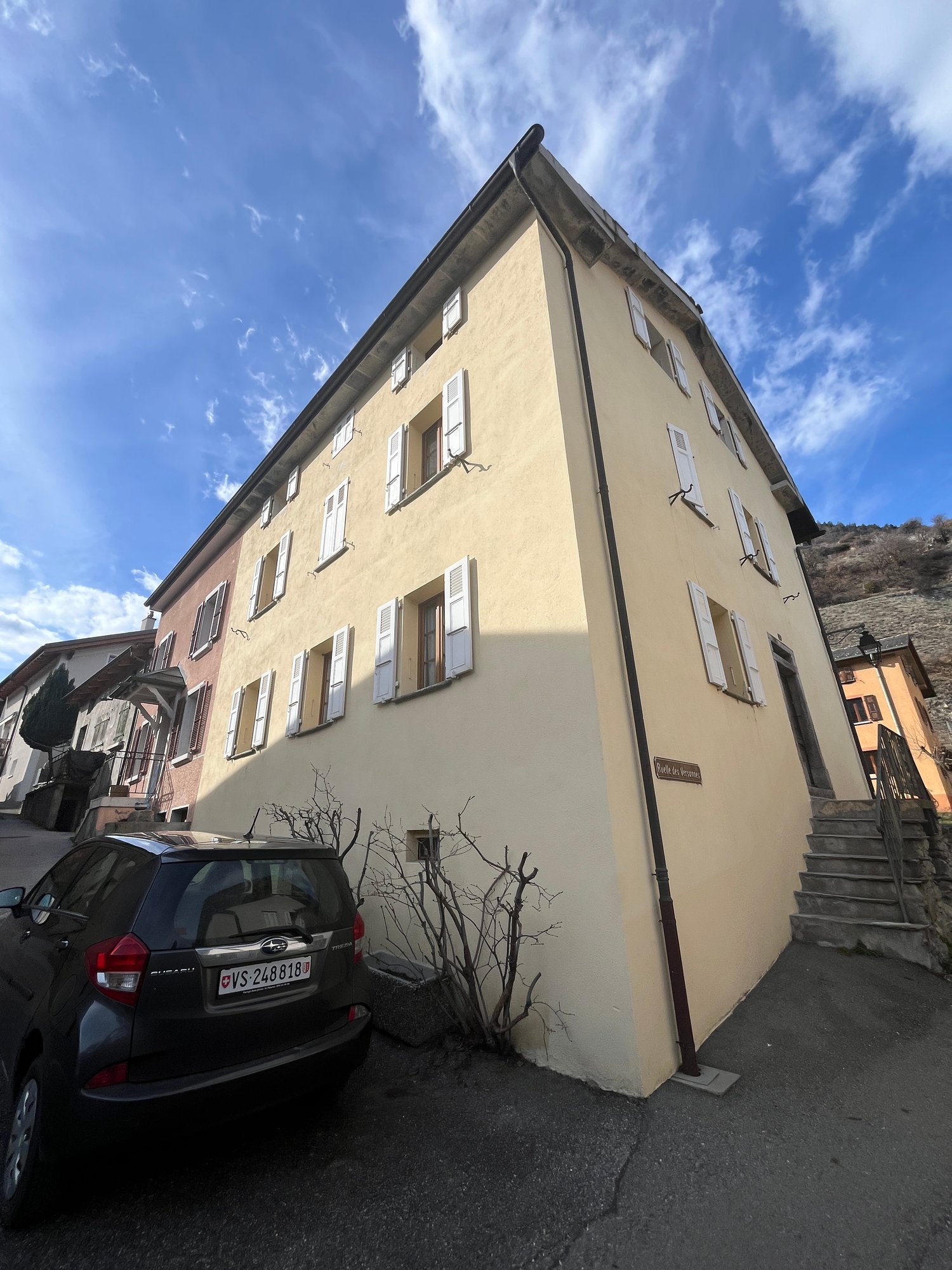 3 story building, beige walls, white windows, black car parked in front