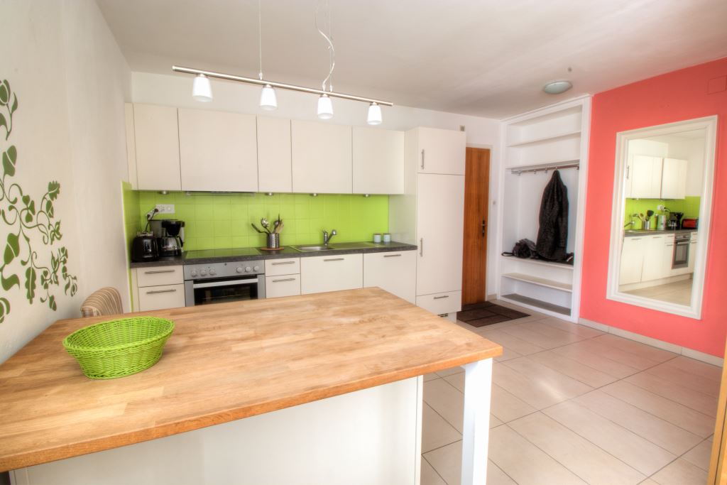 Kitchen with kitchen island, modern white cabinets, green kitchen backsplash, tile flooring, modern overhead lighting, various kitchen appliances