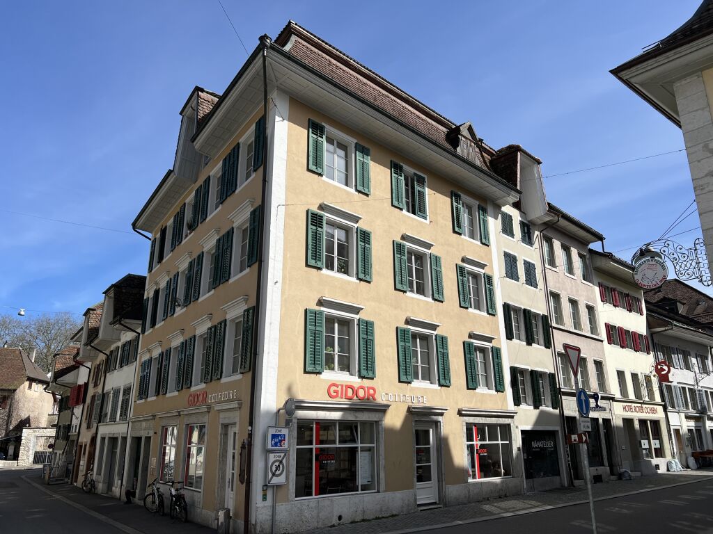 3 story building, beige wall, green shutters, storefronts, bicycles