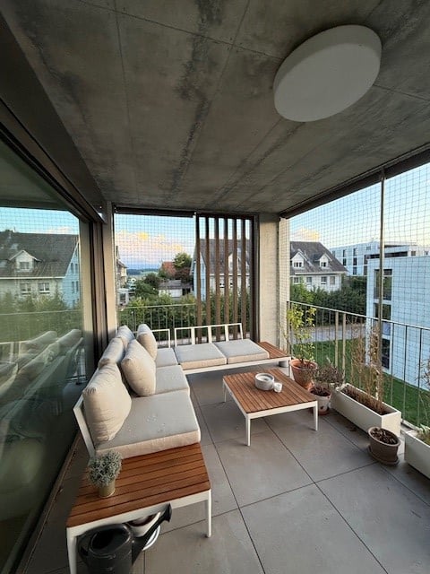 Modern balcony with white couches, wooden coffee table, and large glass windows