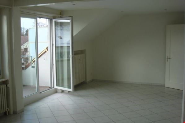 An empty room with a white floor, white walls, a sliding glass door to a balcony, and a white radiator.