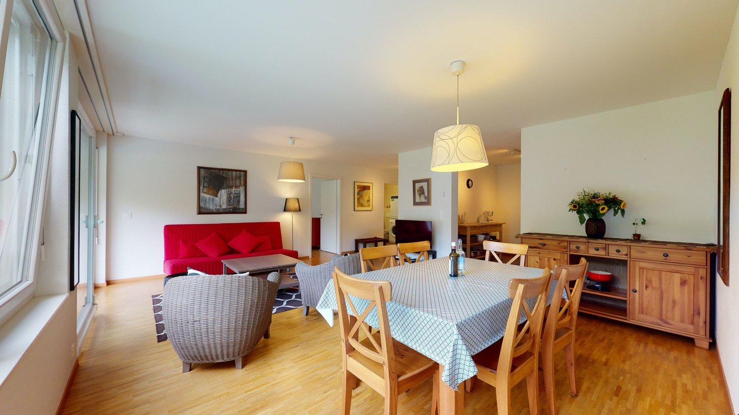 modern dining area, wooden dining table, wooden chairs, red sofa, floor lamp, window, picture frames, cabinet, tableware, flowers