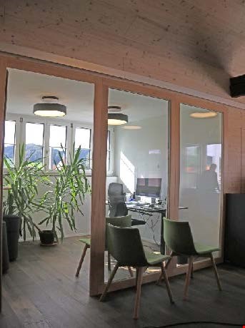 room with desk and monitors, green chairs, large windows, plants, wooden floor